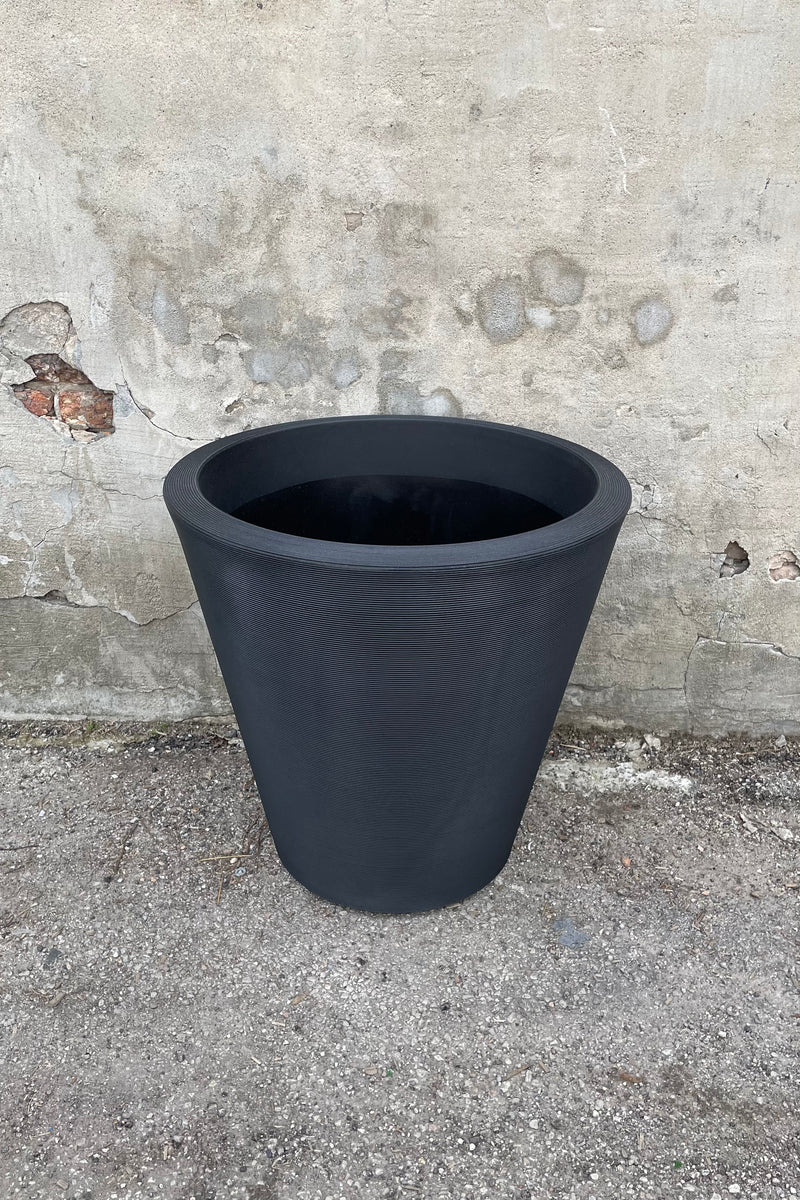 The Madison 26" container in Caviar Black against a concrete wall., 