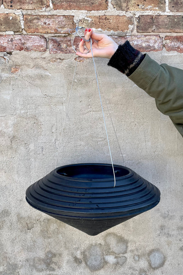 An empty Daniel hanging planter in caviar black against a concrete wall. 