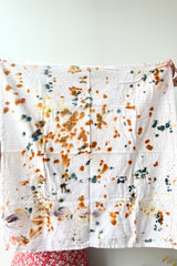 A woman holds an unfolded Botanically Dyed Tea Towel in abstract multi color against a white backdrop