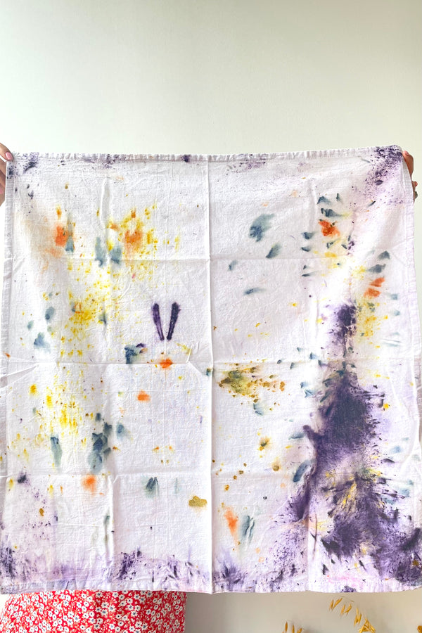 A woman holds an unfolded Botanically Dyed Tea Towel in abstract purple against a white backdrop