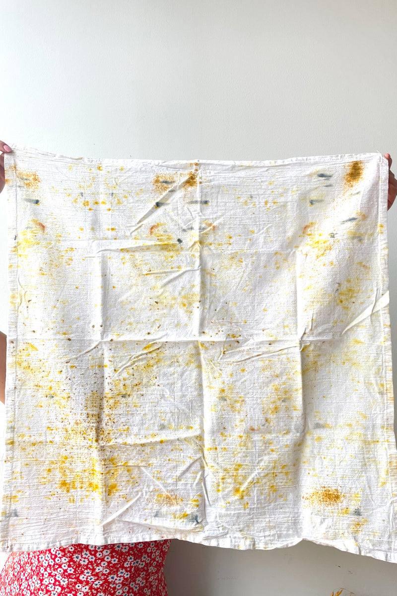 A woman holds an unfolded Botanically Dyed Tea Towel in abstract yellow against a white backdrop