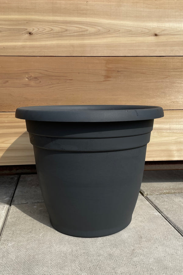 The charcoal Emma round 16" planter shown from the side against a cedar wall. 