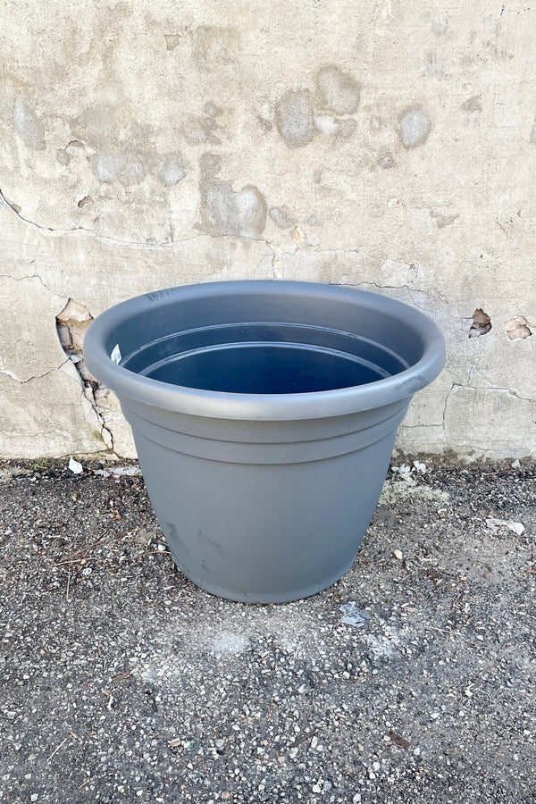 The emma round charcoal 25" planter against a concrete wall. 
