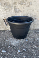 The 25" black Emma round planter against a cement wall. 