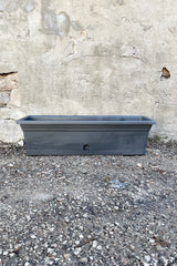 The Emma rectangular charcoal grey 24" planter shown against a concrete wall. 