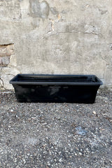 The black emma rectangular planter 24" against a concrete wall. 