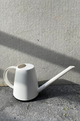 white Cleo watering can against a grey wall. 