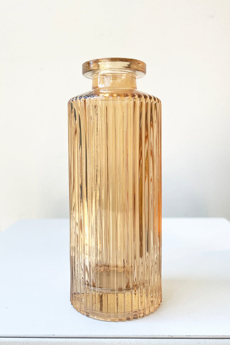A frontal view of the Amber Pleated Glass Bottle Bud Vase against a white backdrop
