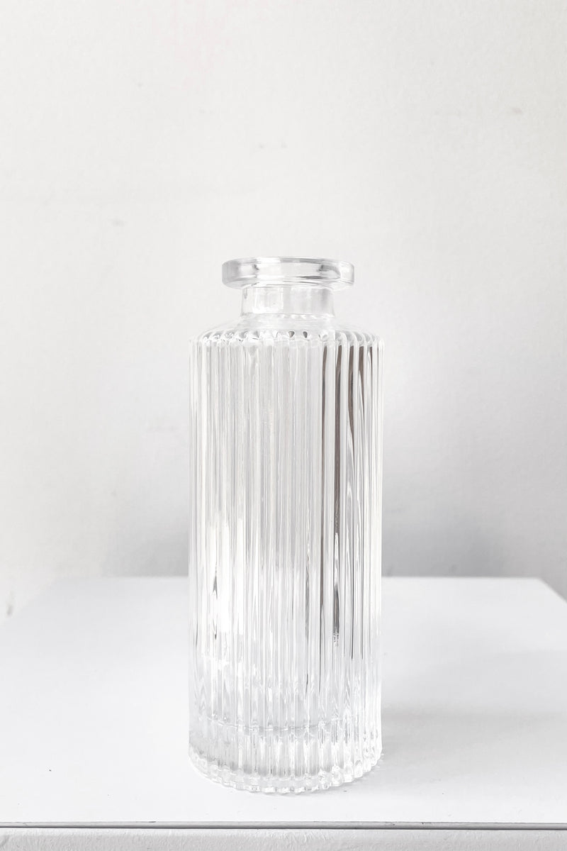 A frontal view of the Pleated Medicine Bud Vase in Clear against a white backdrop
