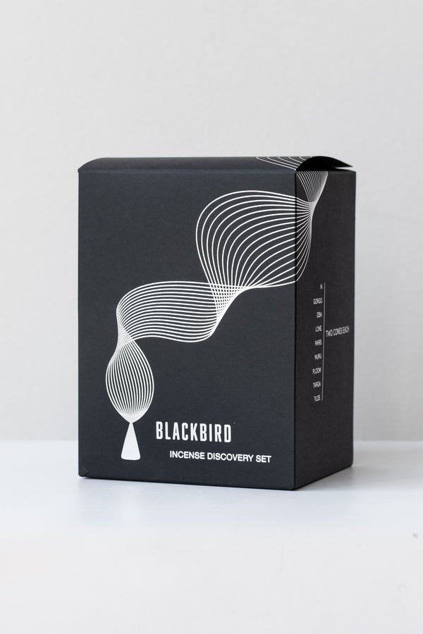 The Blackbird Incense Discovery set sits on a white table in a white room. The box is black with a minimalist design of a burning incense cone in white.