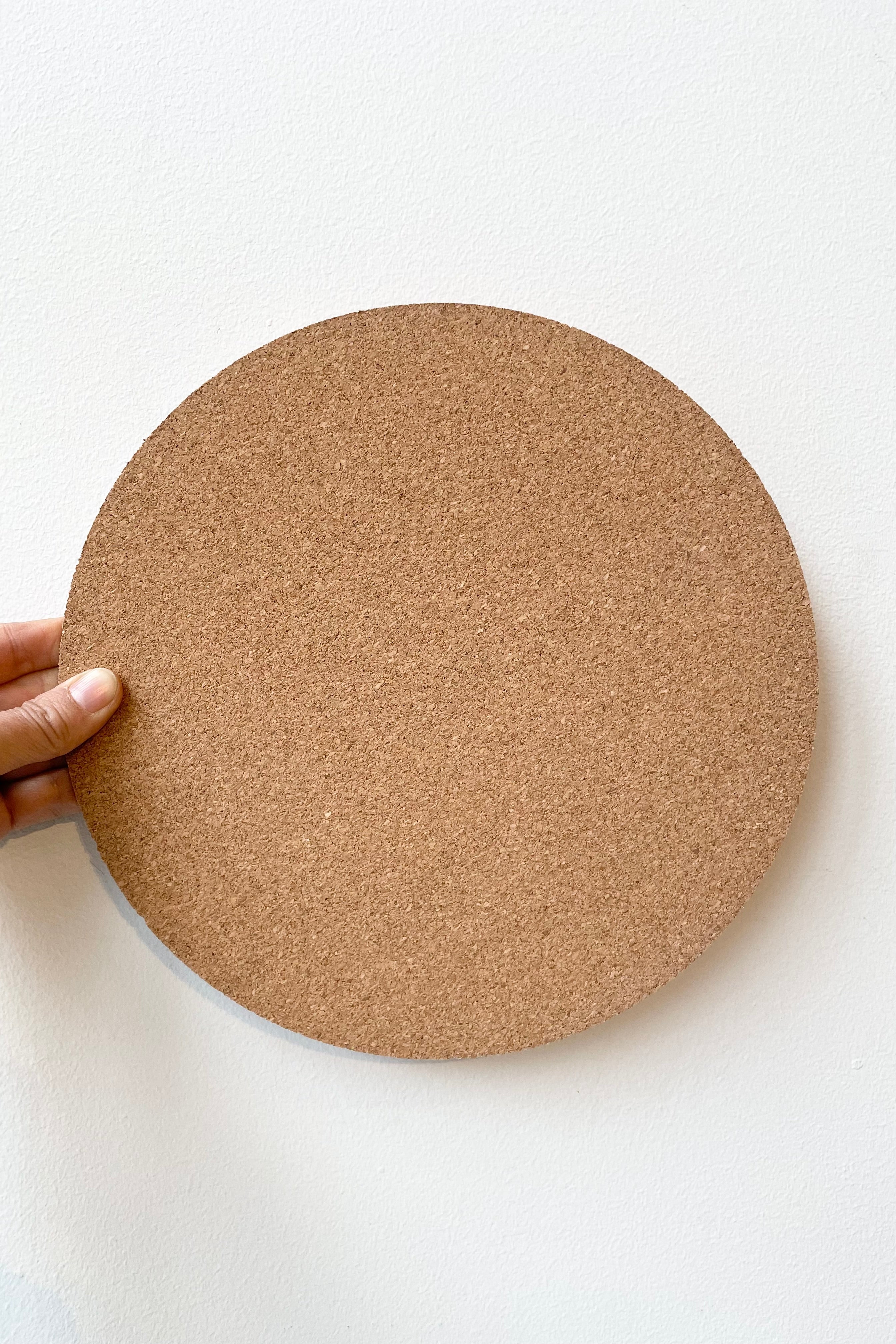 The 10" diameter Dotchi cork mat being held against a white wall with the cork top facing the camera.