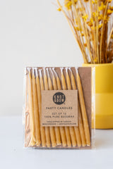 Natural short beeswax birthday party candles by knot and bow in front of yellow dried floral arrangement