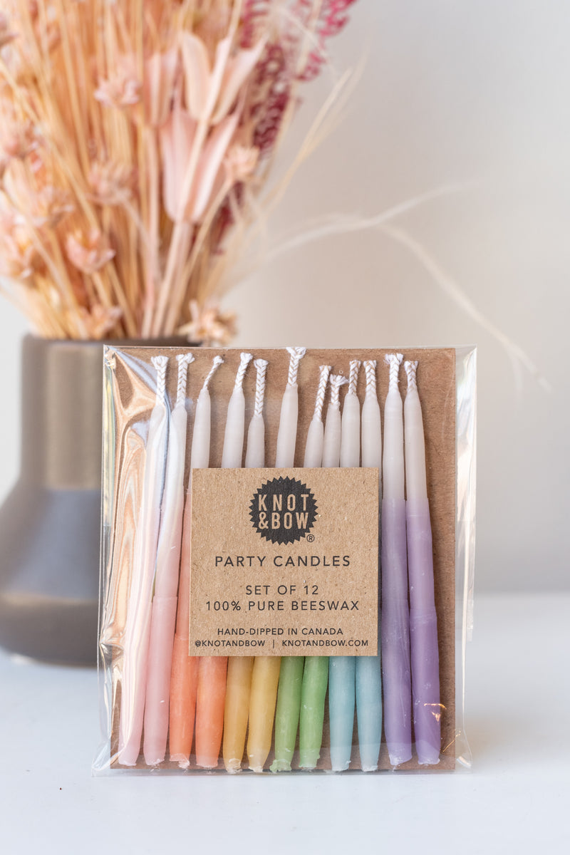 Ombre short assorted beeswax birthday party candles by knot and bow in front of dried peachy floral arrangement