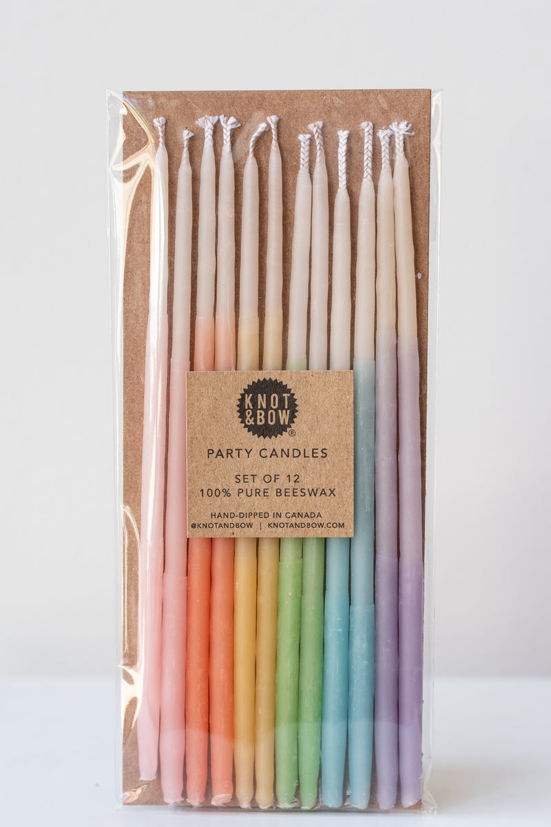 Tall ombre assorted beeswax birthday party candles by knot and bow in front of white background