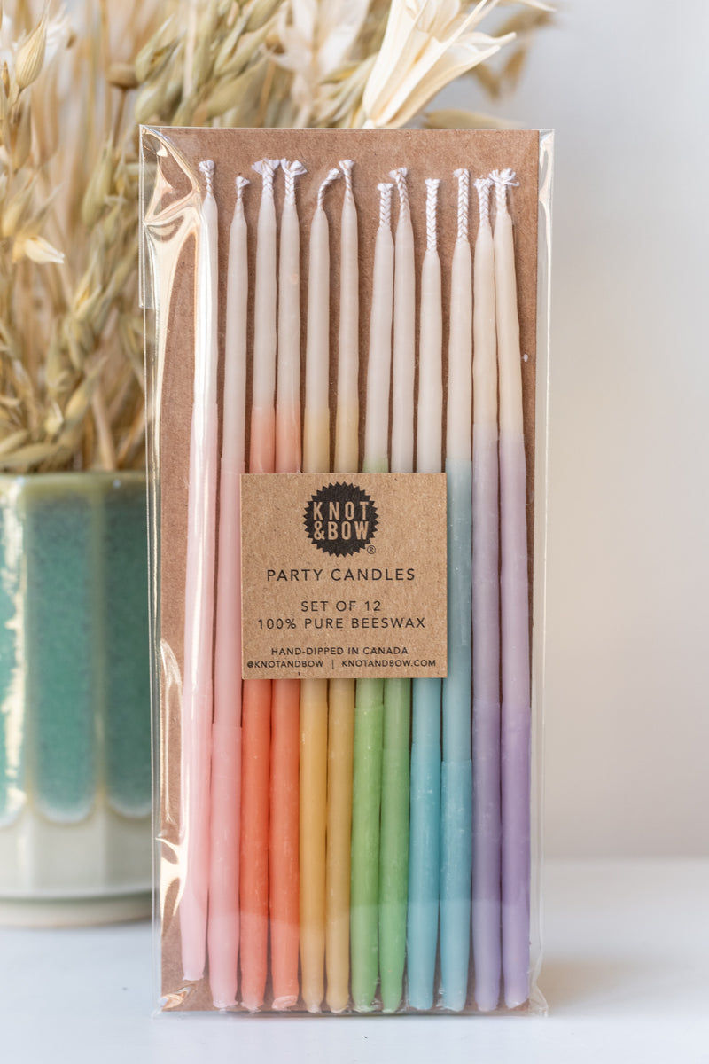 Tall ombre assorted beeswax birthday party candles by knot and bow in front of natural dried floral arrangement