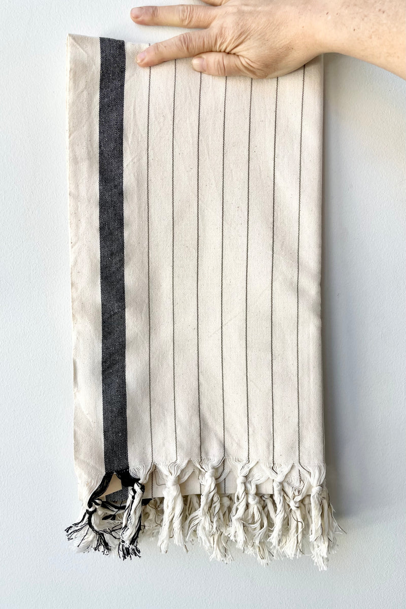 The Bodrum hammam towel folded being held against a white wall at Sprout Home. 