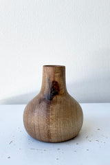 The walnut Nina wood vase against a white wall at Sprout Home.