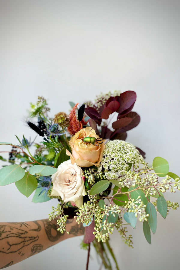 Betelgeuse arrangement with shades of gray and hints of dark foliage and white flowers with a beetle on one of the roses designed by Sprout Home.