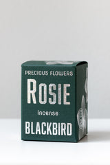 Rosie incense by BLACKBIRD sits on a white surface in a white room