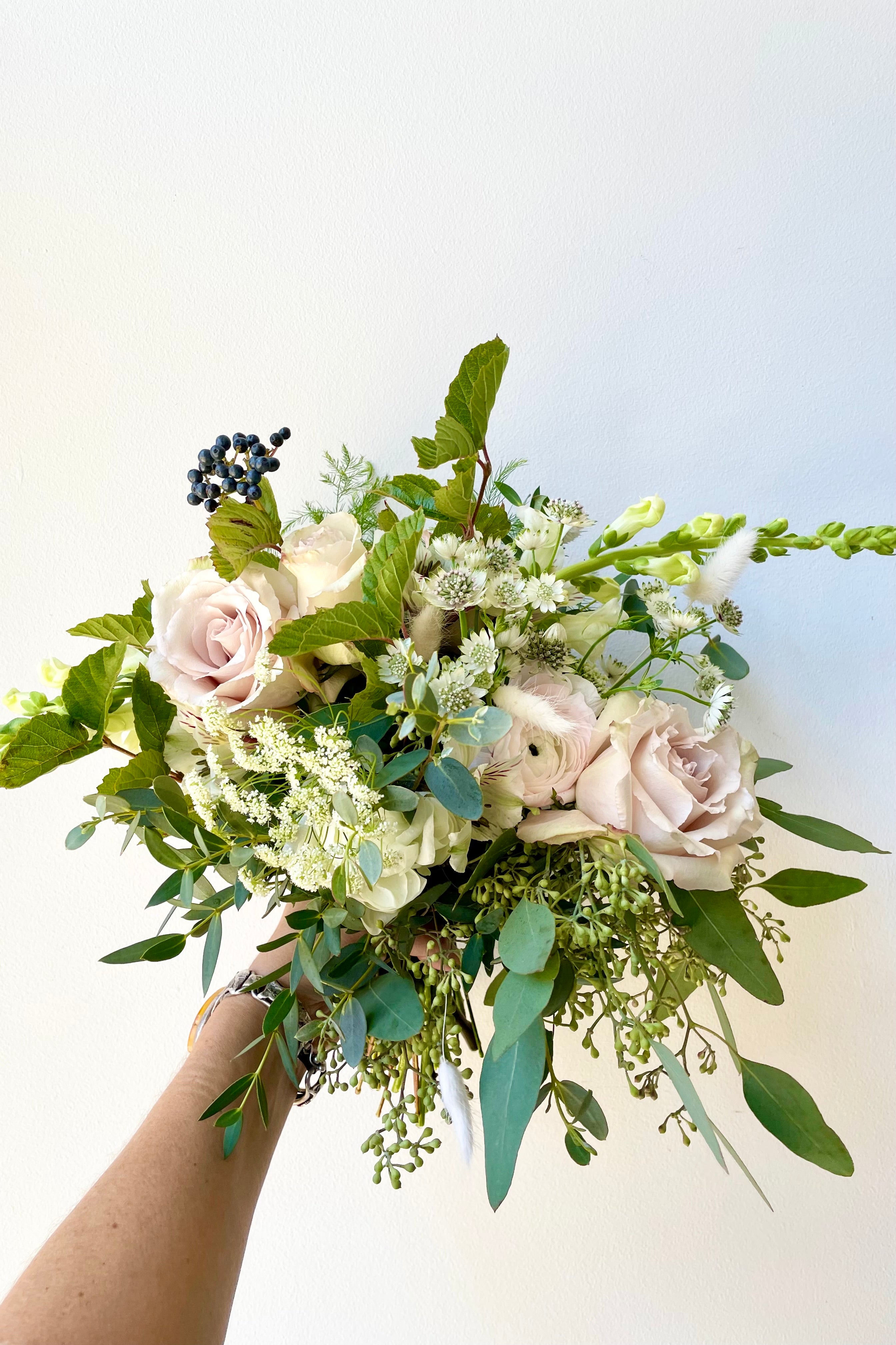 A hand holds Fresh Floral Arrangement Bleached from Sprout Home against a white backdrop #size_$90