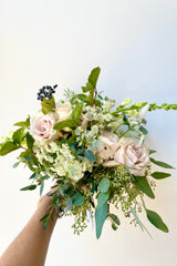 A hand holds Fresh Floral Arrangement Bleached from Sprout Home against a white backdrop