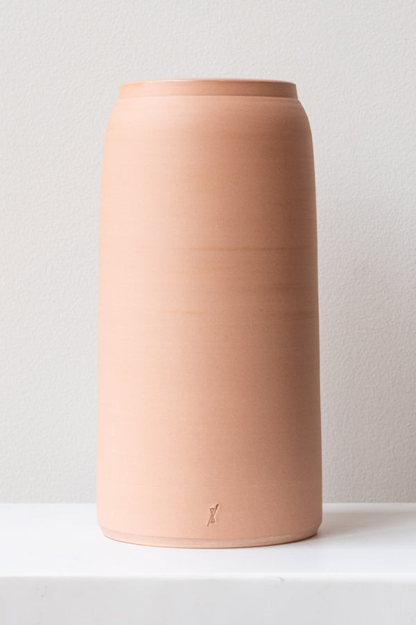 One large pink ceramic bouquet vase sits on a white surface in a white room. The vase is empty. It is photographed straight on.