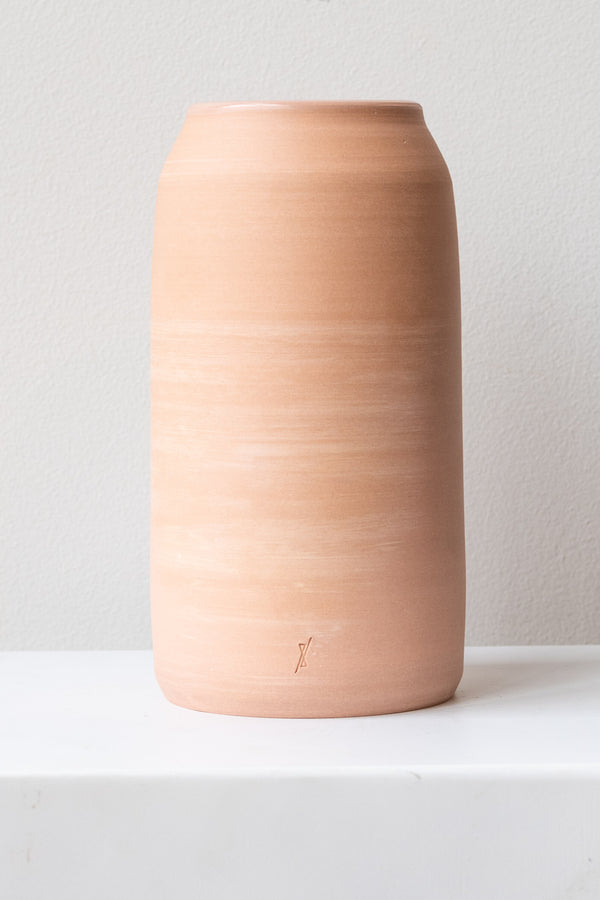 One medium pink ceramic bouquet vase sits on a white surface in a white room. The vase is empty. It is photographed straight on.