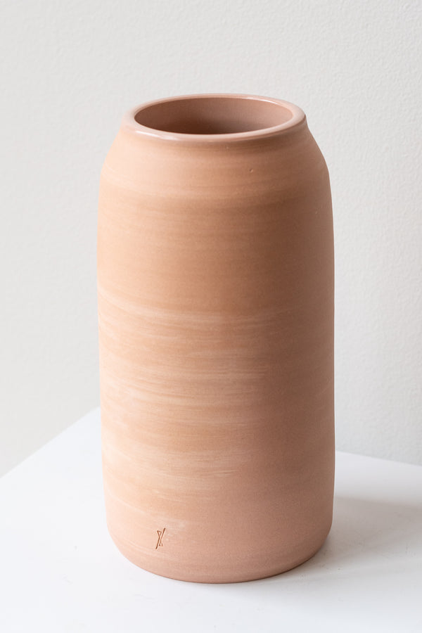 One medium pink ceramic bouquet vase sits on a white surface in a white room. The vase is empty. It is photographed closer and at an angle.
