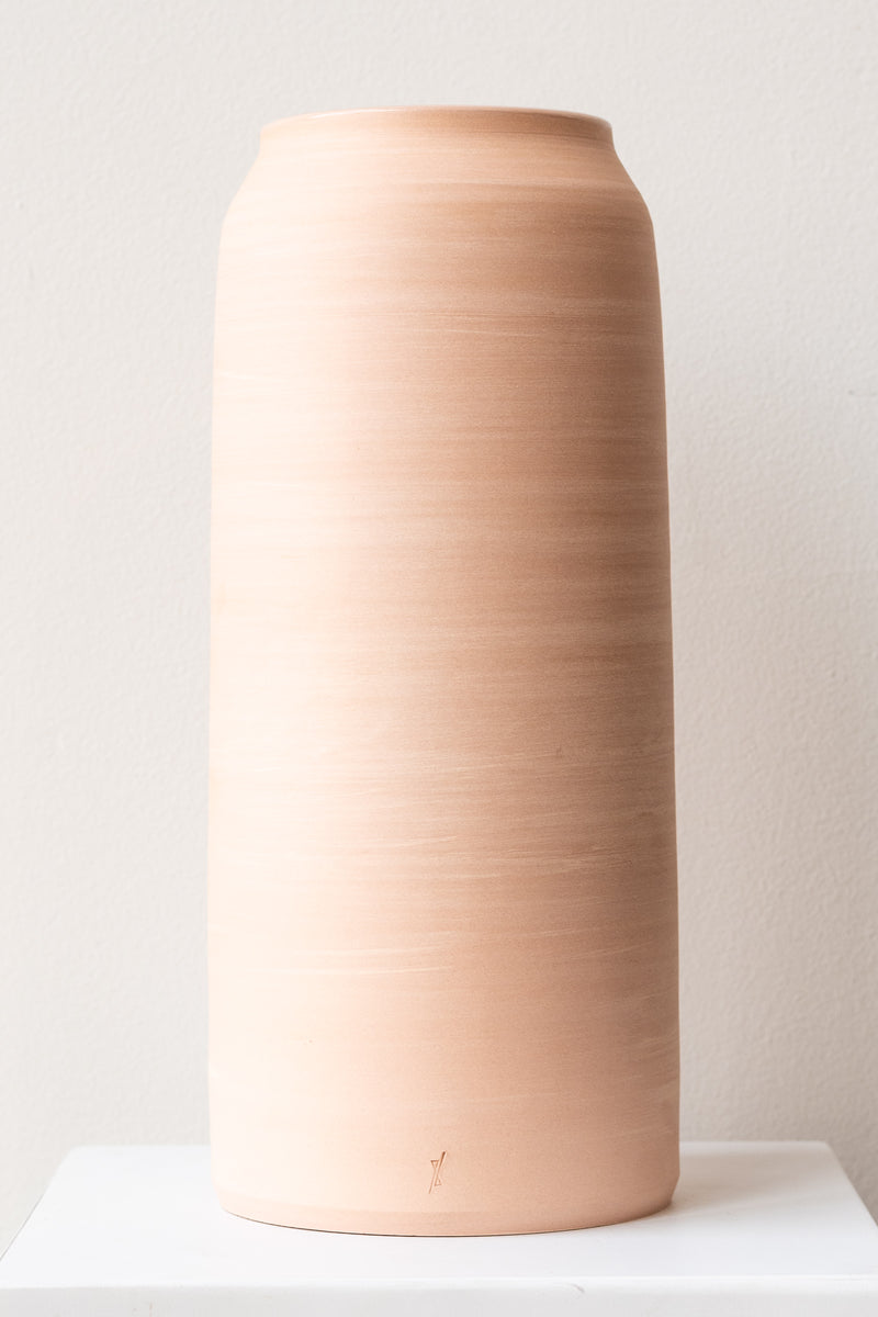 One extra extra large pink ceramic bouquet vase sits on a white surface in a white room. The vase is empty. It is photographed straight on.