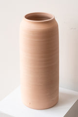 One extra extra large pink ceramic bouquet vase sits on a white surface in a white room. The vase is empty. It is photographed closer and at an angle.