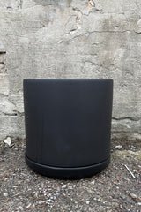 The 10" solid cylinder and saucer in black against a concrete wall. 