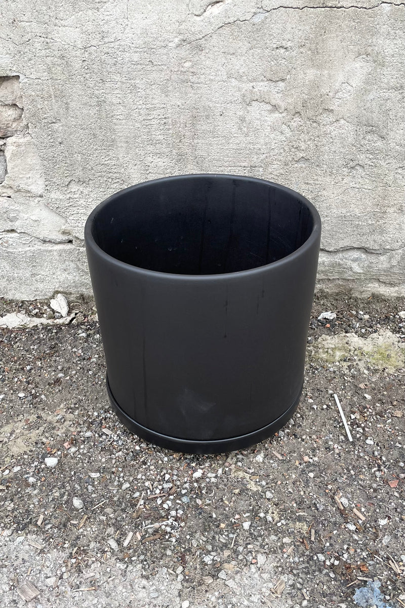 The 10" solid cylinder and saucer in black against a concrete wall. 