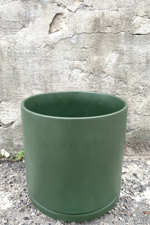A slight over-the-lip view of the 10" solid cylinder and saucer in forest green against a concrete backdrop