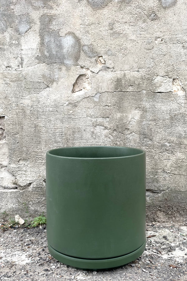 A frontal view of the 10" solid cylinder and saucer in forest green against a concrete backdrop