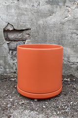 10" rust solid cylinder and saucer against a cement wall. 
