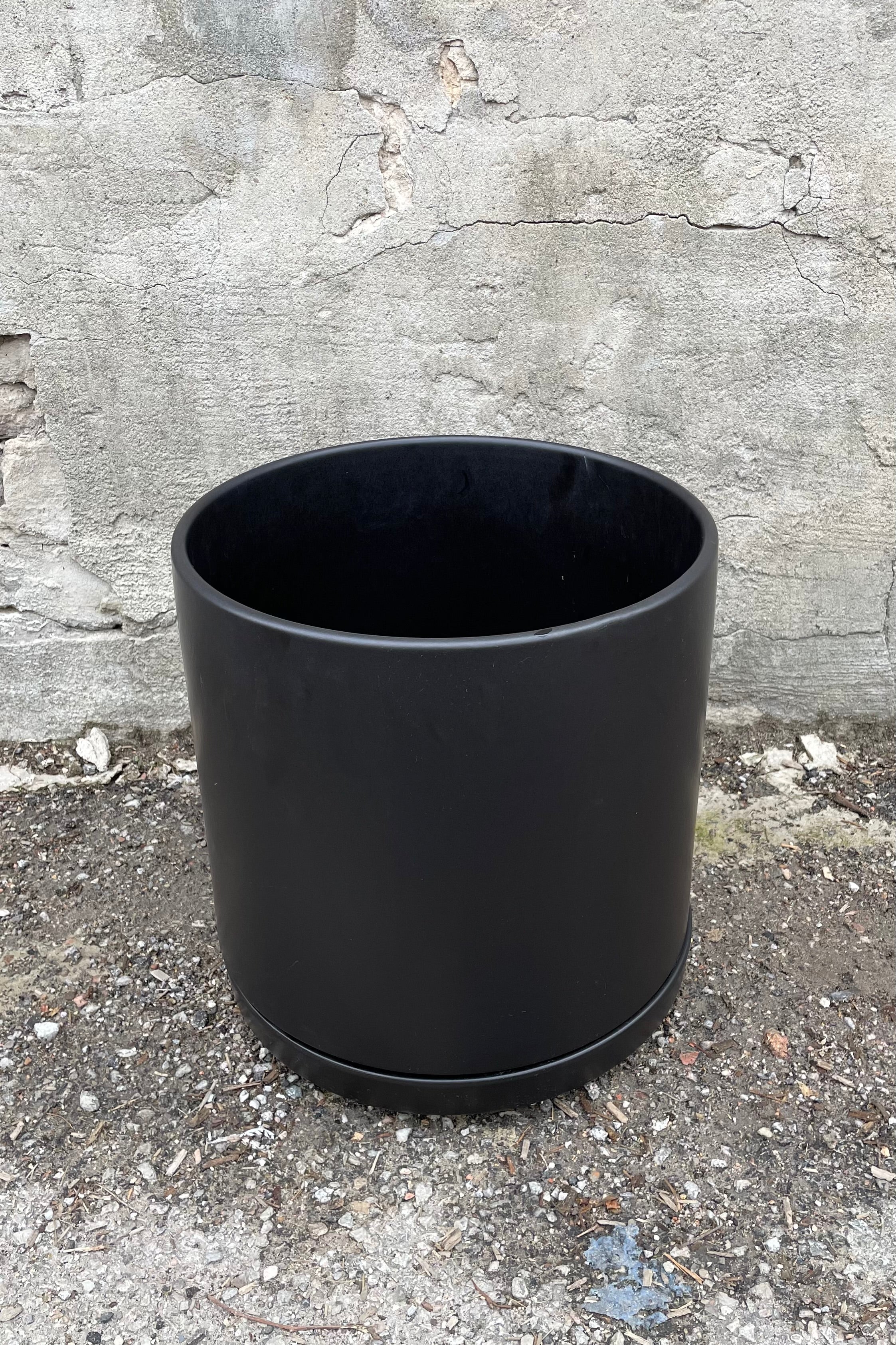The black solid cylinder and saucer against a cement wall. 
