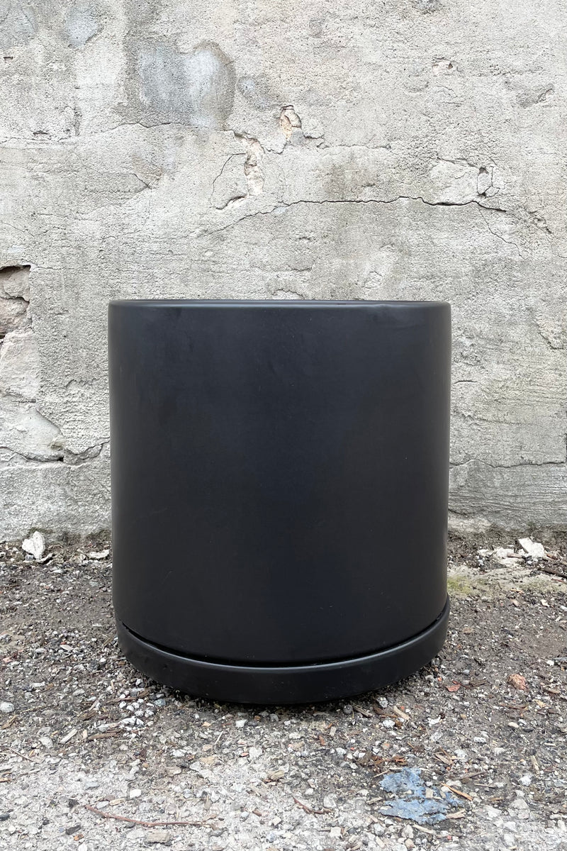 The black solid cylinder and saucer against a cement wall. 