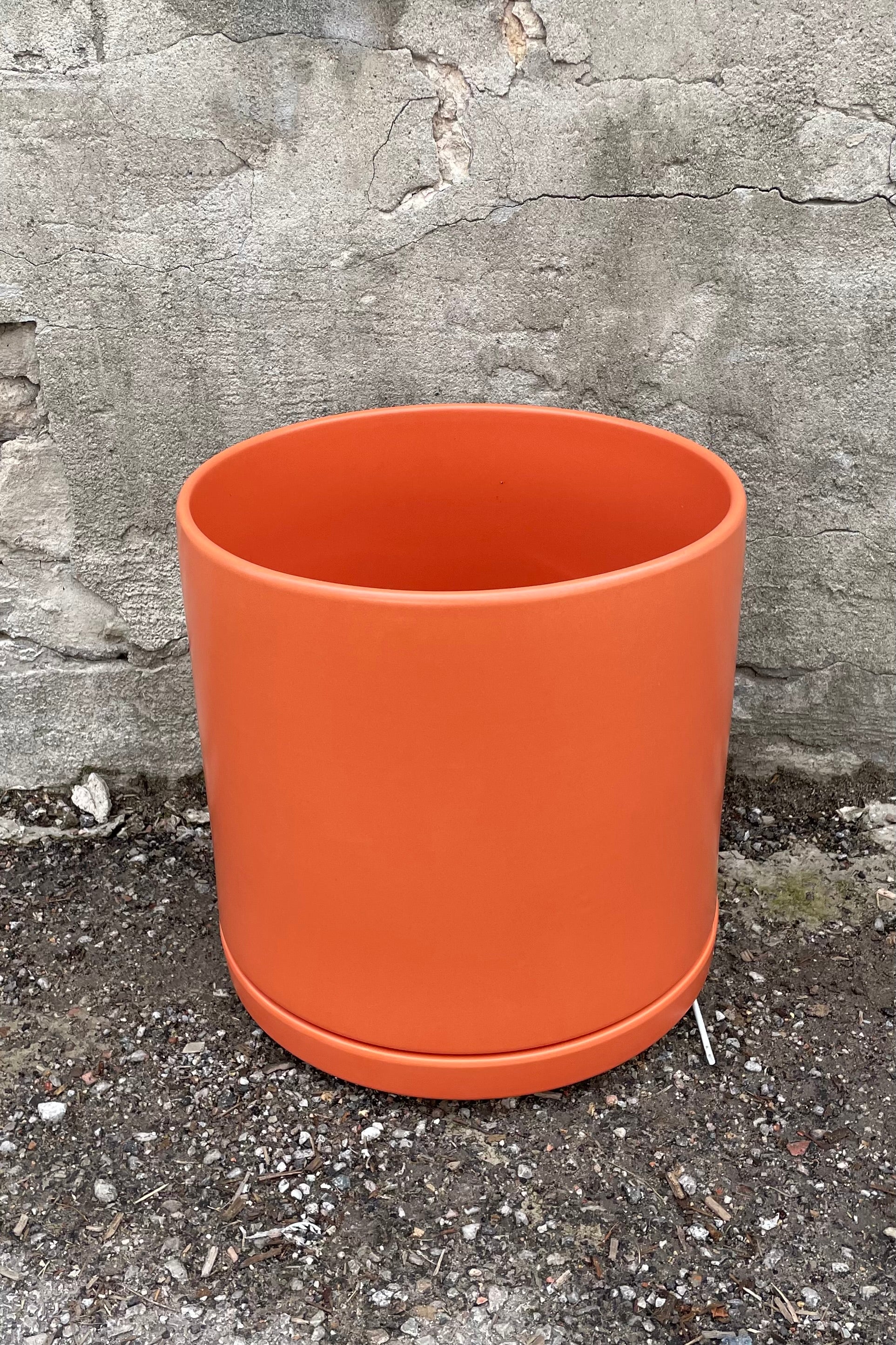 12" rust solid cylinder and saucer against a cement wall. 