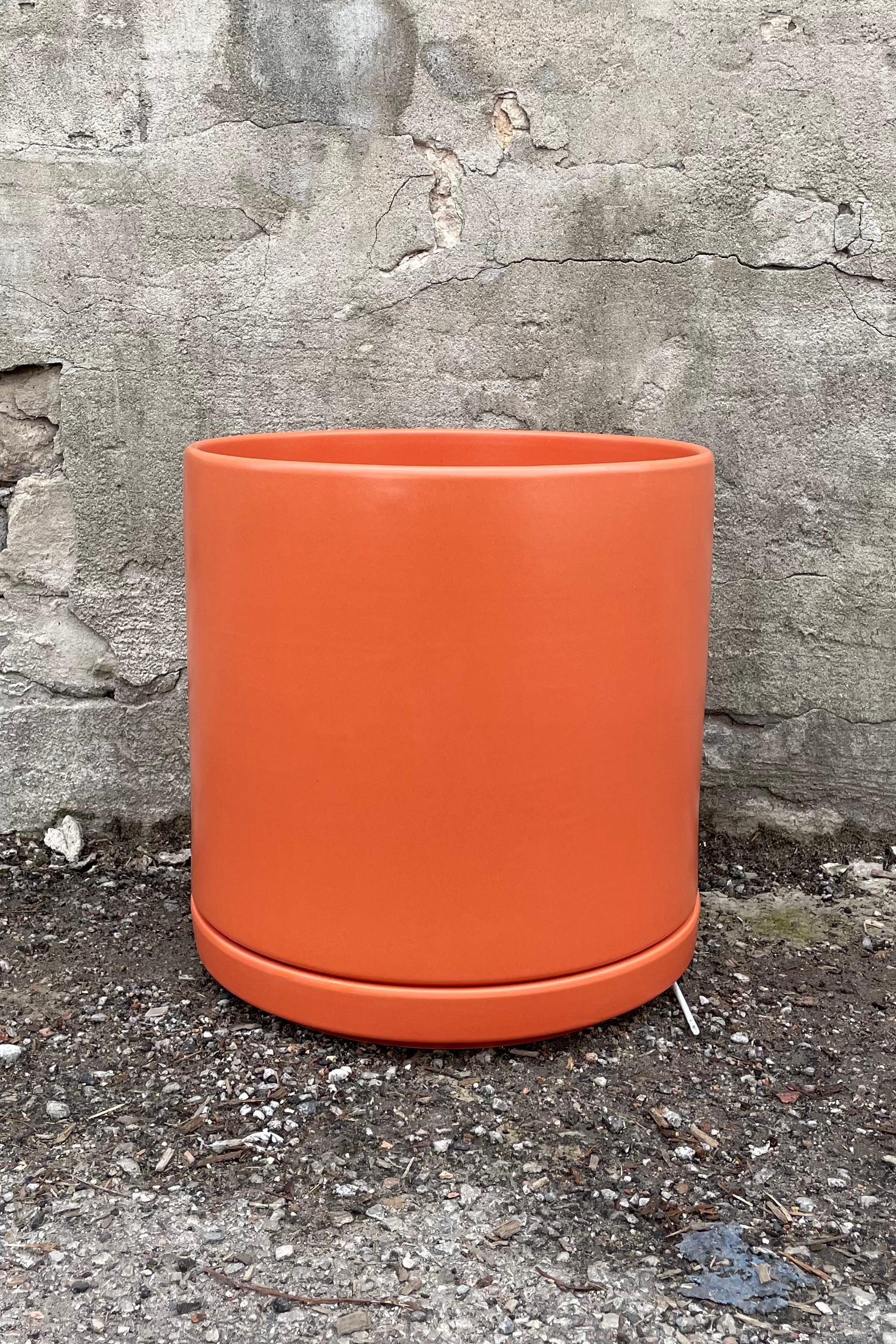 12" rust solid cylinder and saucer against a cement wall. 