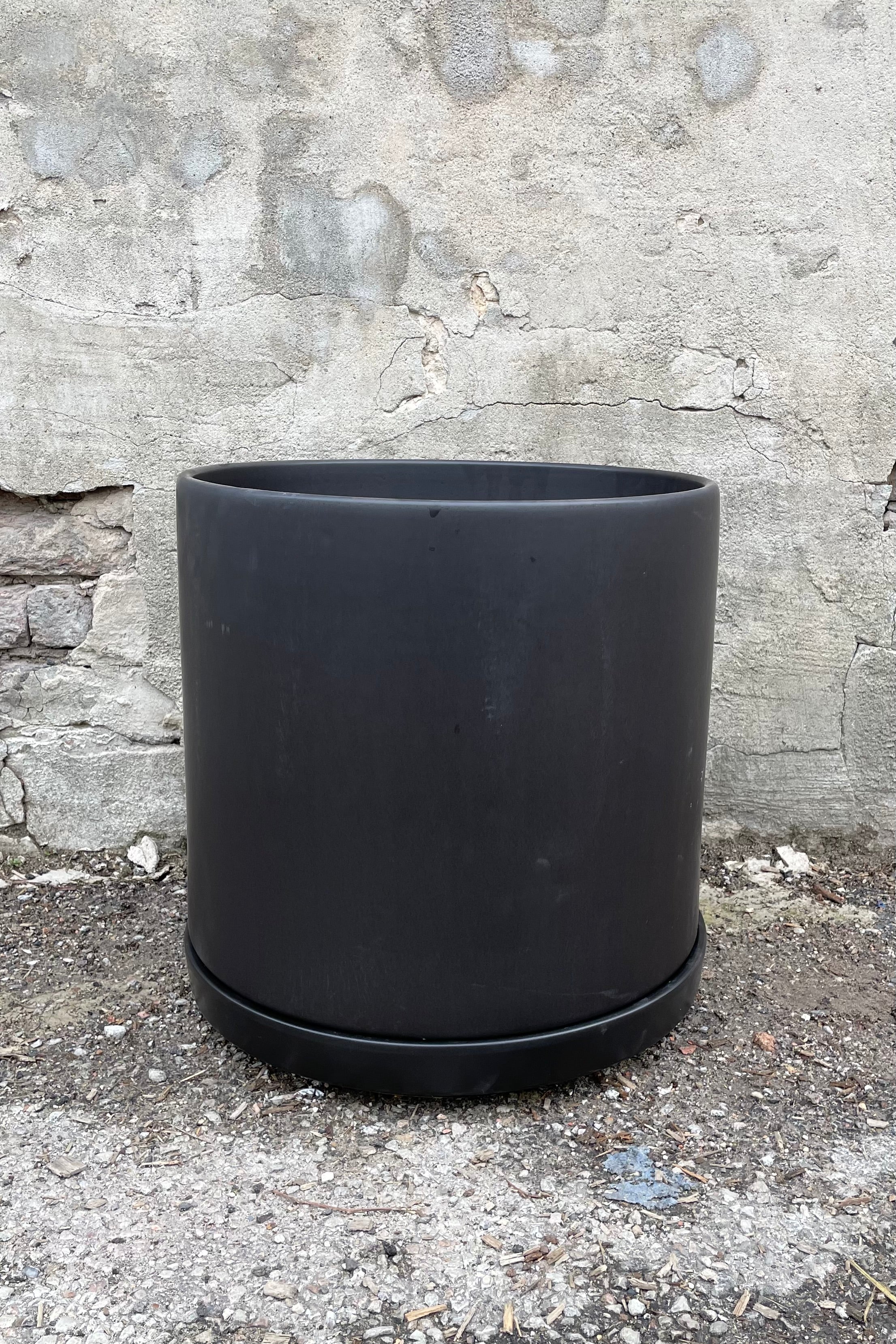 The 15" black solid cylinder and saucer against a concrete wall.  