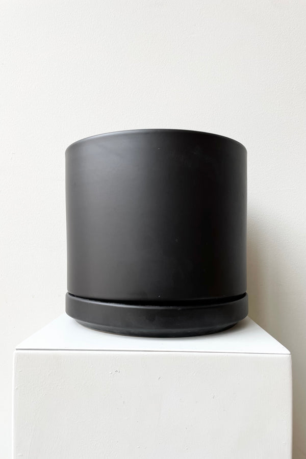 Solid Cylinder & Saucer black 8” against a white wall