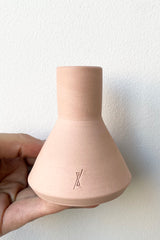 The L'Impatience coral colored ceramic taper candle holder being held in hand against a white wall at Sprout Home.