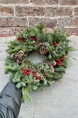 The Deluxe candle red ring wreath held against a concrete wall.