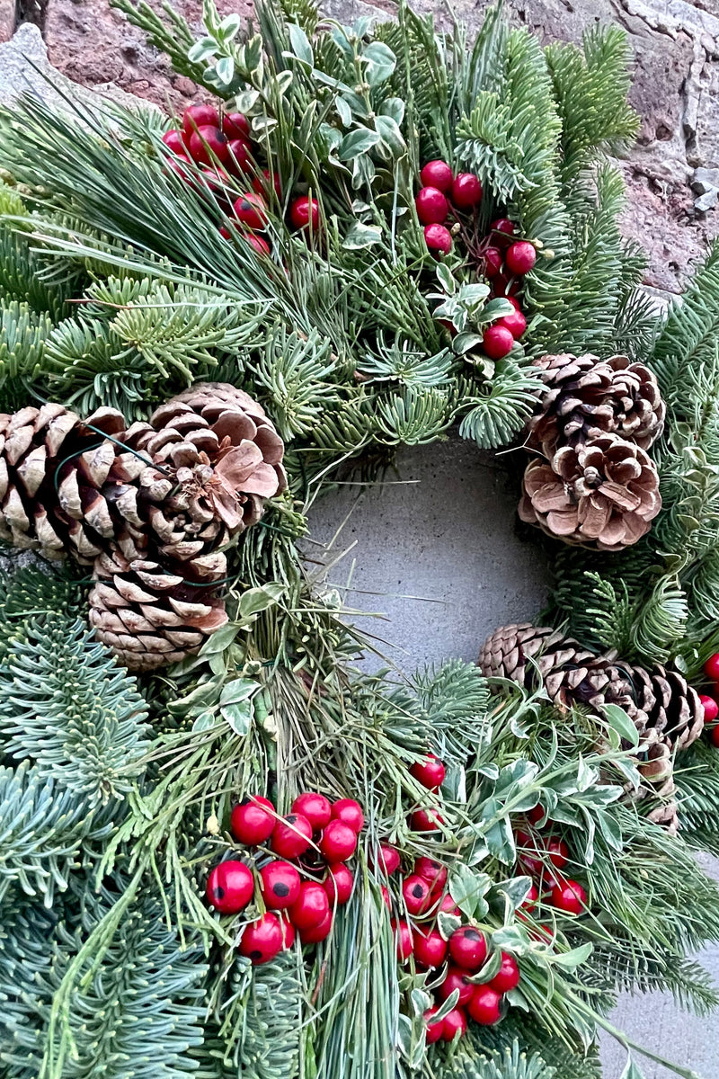 A detail picture of the deluxe red candle ring wreath showing the faux red berries and pine cones