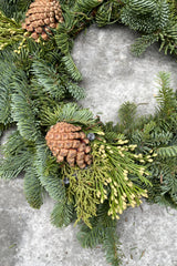 detail pictures of a small candle ring evergreen wreath with pine cone and cedar pieces.