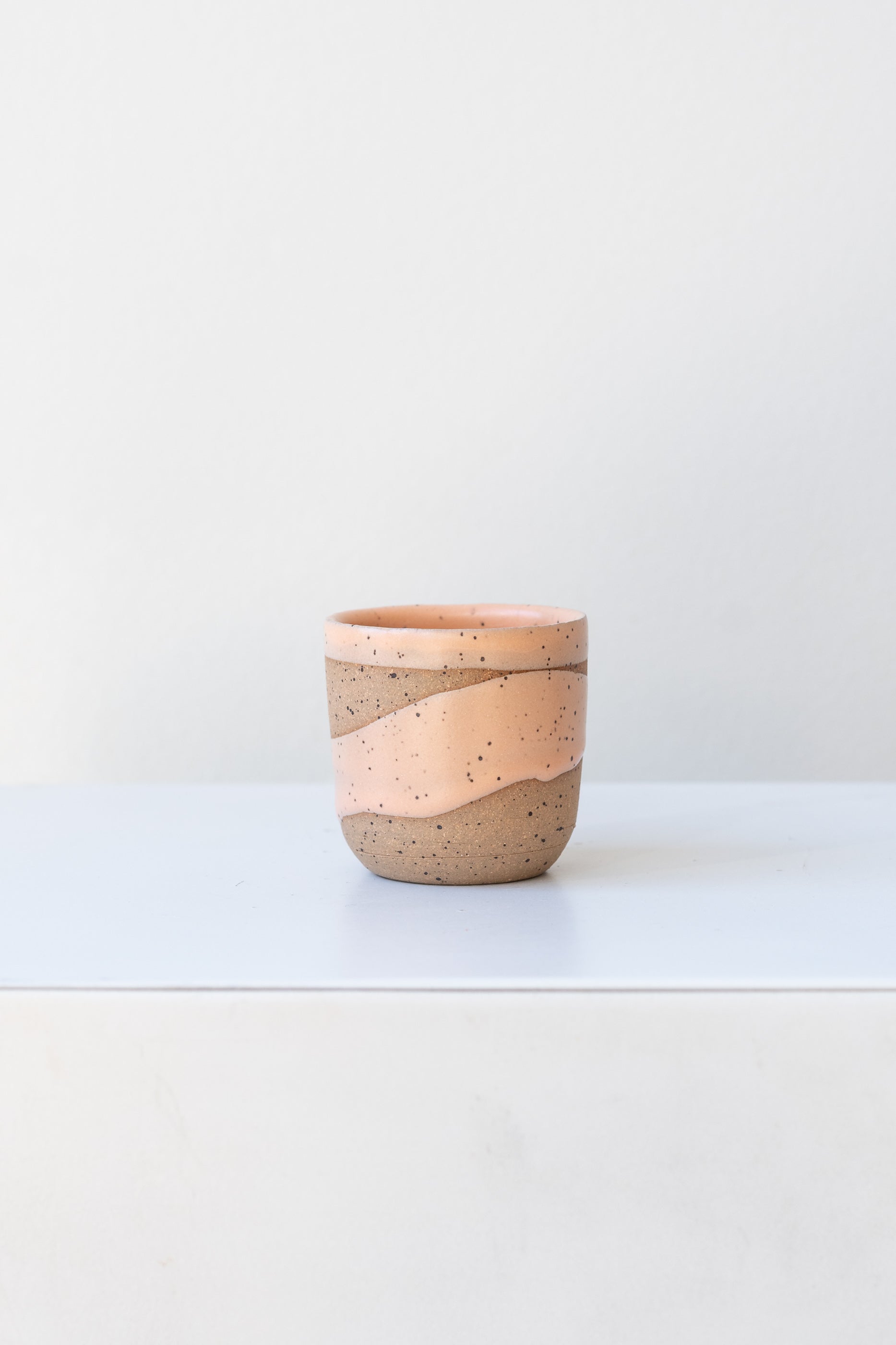 Apricot Coastal Glaze Cup by Christina Kosinski sits on a white surface in a white room