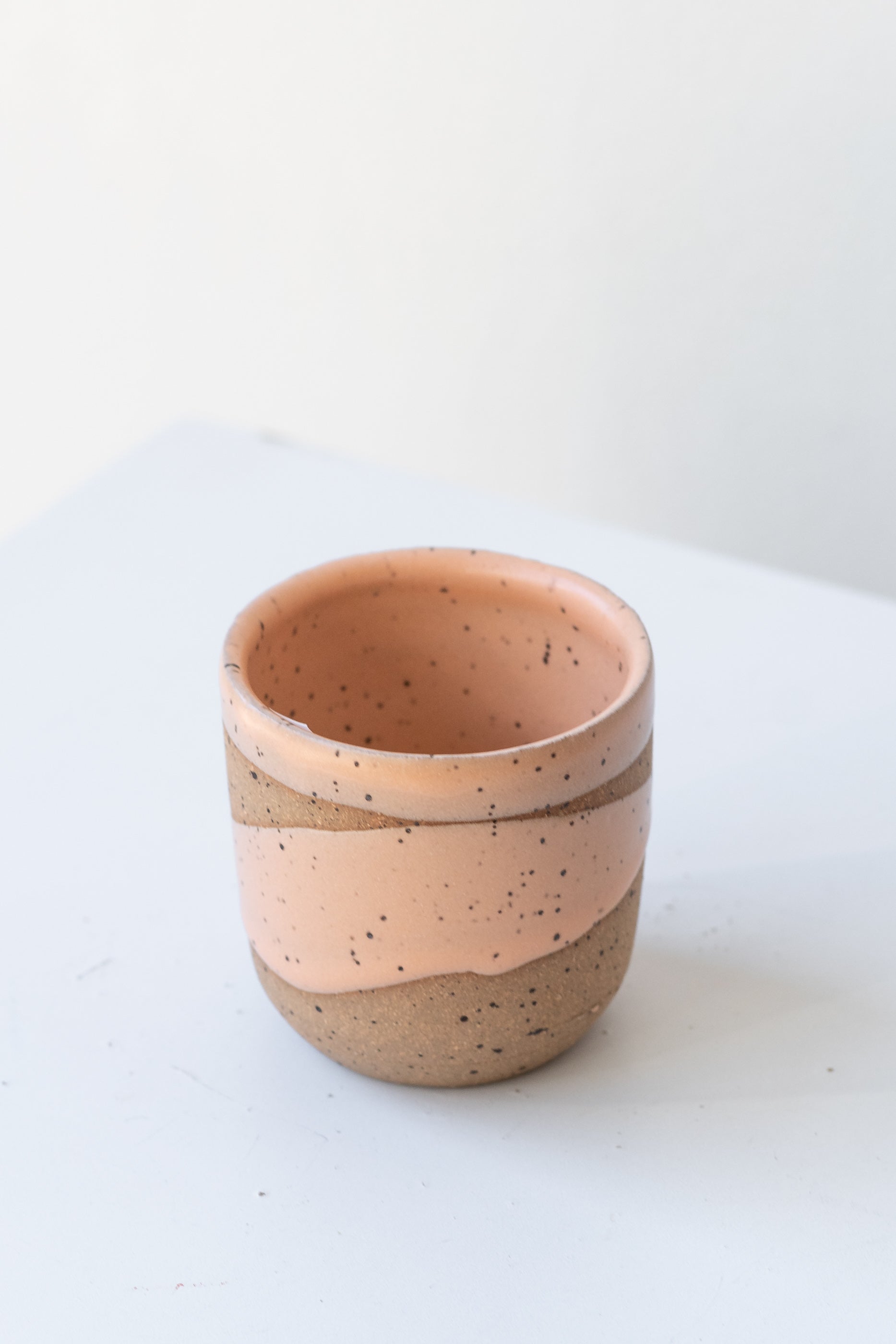 Apricot Coastal Glaze Cup by Christina Kosinski sits on a white surface in a white room