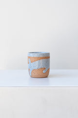 Blue Coastal Glaze Cup by Christina Kosinski sits on a white surface in a white room