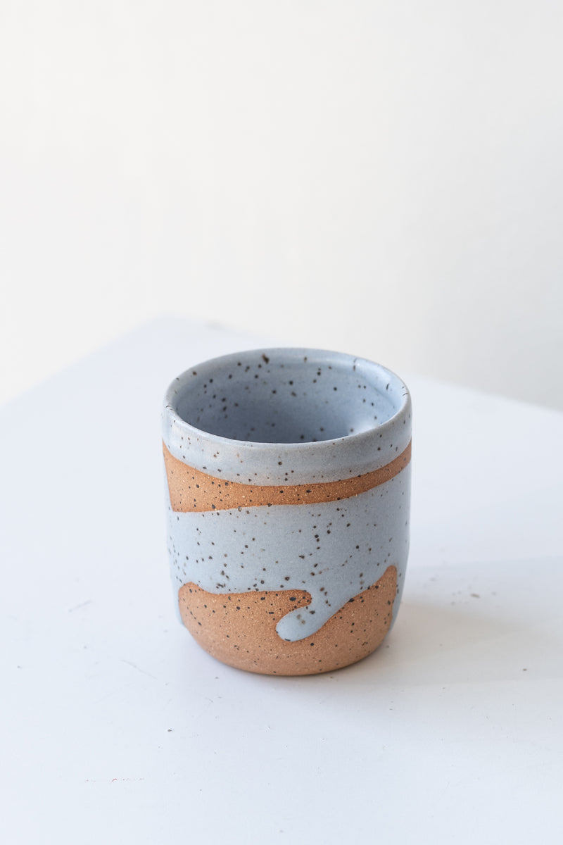 Blue Coastal Glaze Cup by Christina Kosinski sits on a white surface in a white room