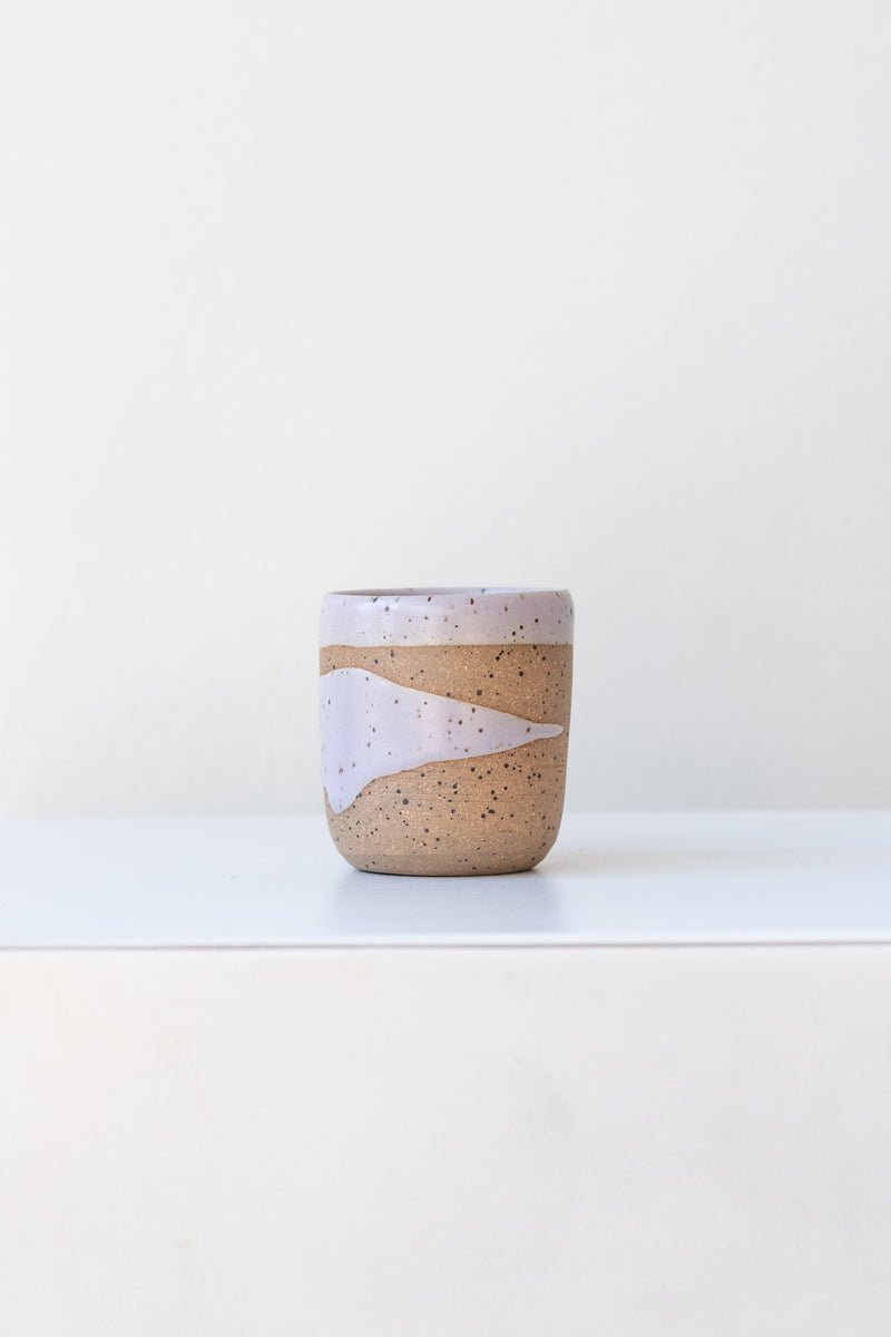 Lavender Coastal Glaze Cup by Christina Kosinski sits on a white surface in a white room